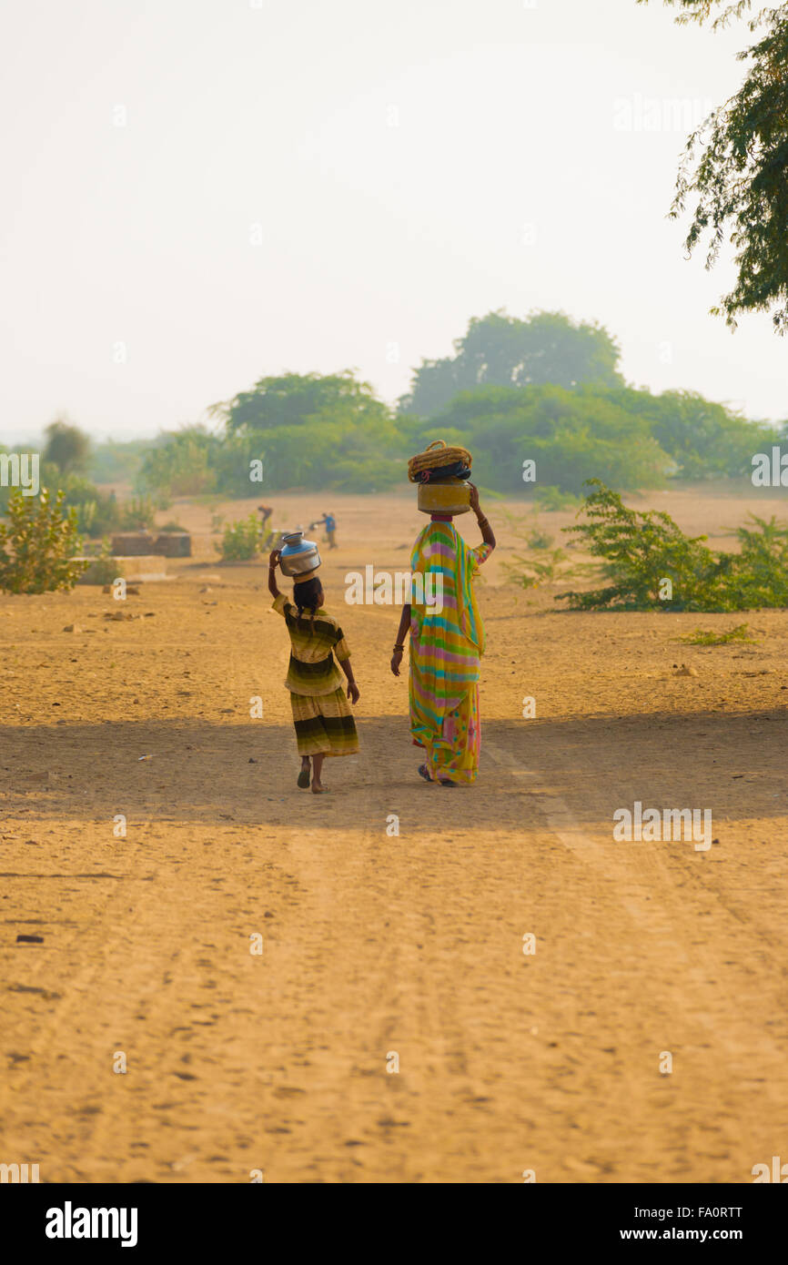 Villaggio rurale Indian madre e figlia il recupero di acqua alla comunità ben caraffe di bilanciamento nel clima secco del deserto su strada sterrata Foto Stock