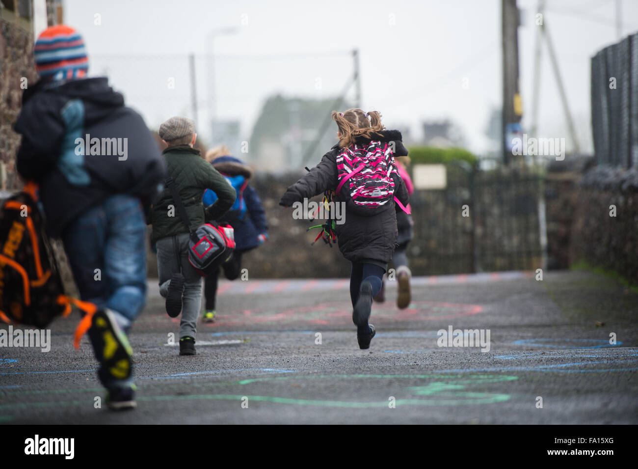 Un gruppo di bambini della scuola primaria focoso precipitando in esecuzione al di fuori della loro piccola scuola rurale alla fine del giorno all'inizio del fine settimana o le vacanze ferie . Wales UK Foto Stock
