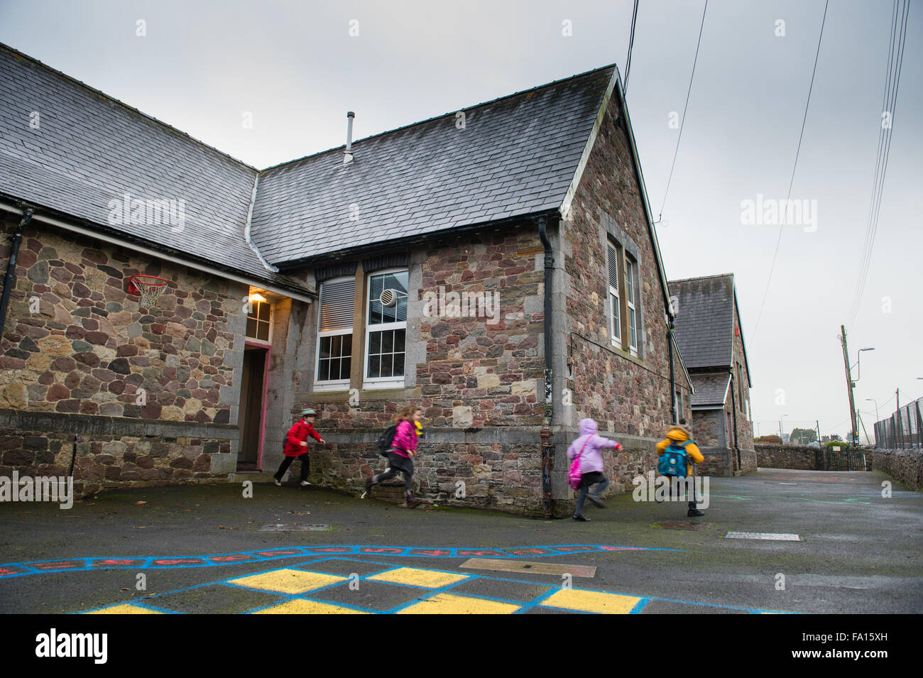 Un gruppo di bambini della scuola primaria focoso precipitando in esecuzione al di fuori della loro piccola scuola rurale alla fine del giorno all'inizio del fine settimana o le vacanze ferie . Wales UK Foto Stock