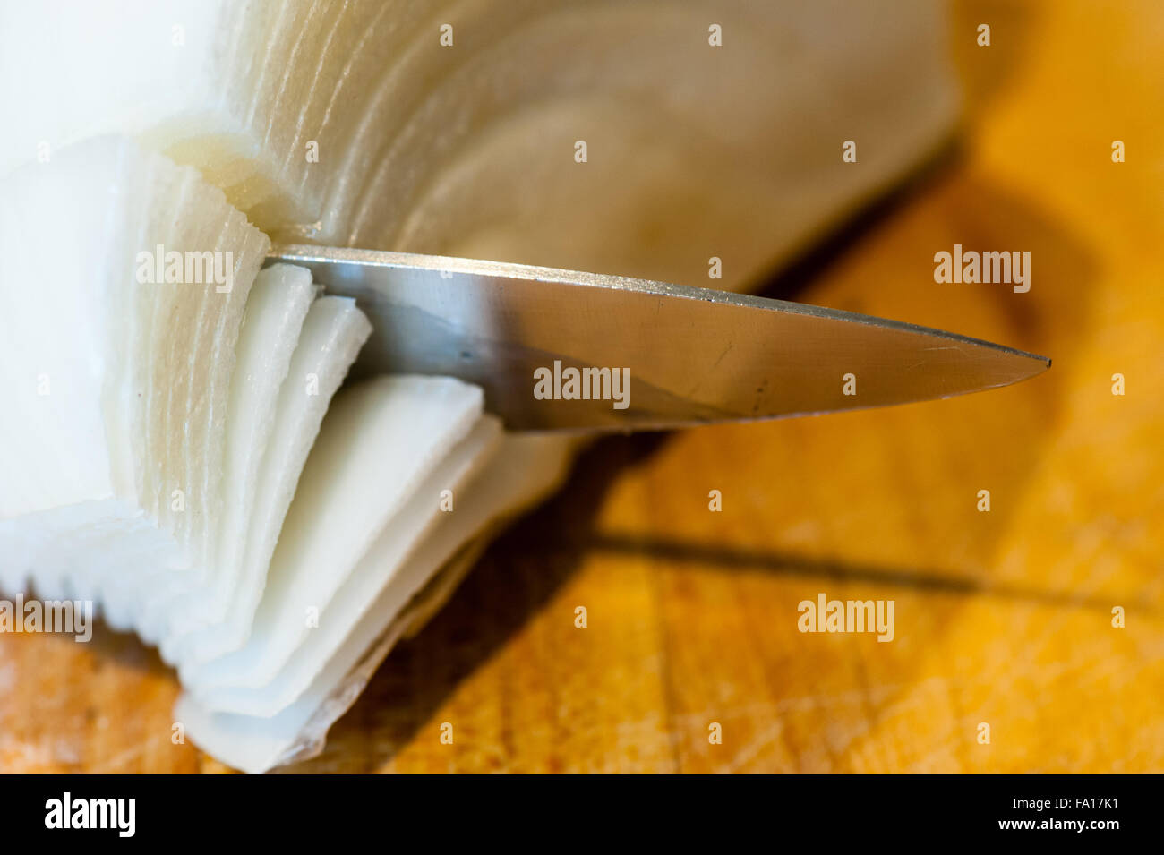 Macro Close-up di punta di metallo appuntito di taglio dei coltelli attraverso strati di cipolla bianca su una superficie di legno. Foto Stock
