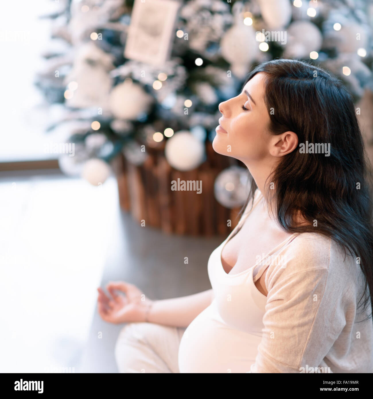 Un sano donna incinta facendo esercizi yoga a casa nel periodo di Natale, con gli occhi chiusi in seduta lotus pongono e meditazione Foto Stock