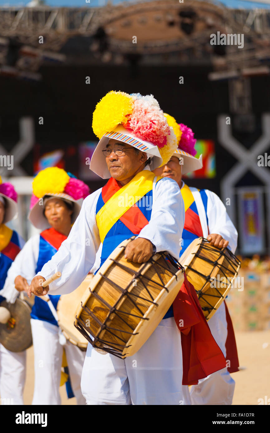 Un vecchio uomo senior di riproduzione di un tradizionale coreano tamburo tenute insieme con corda in abiti colorati in un locale festival all'aperto Foto Stock