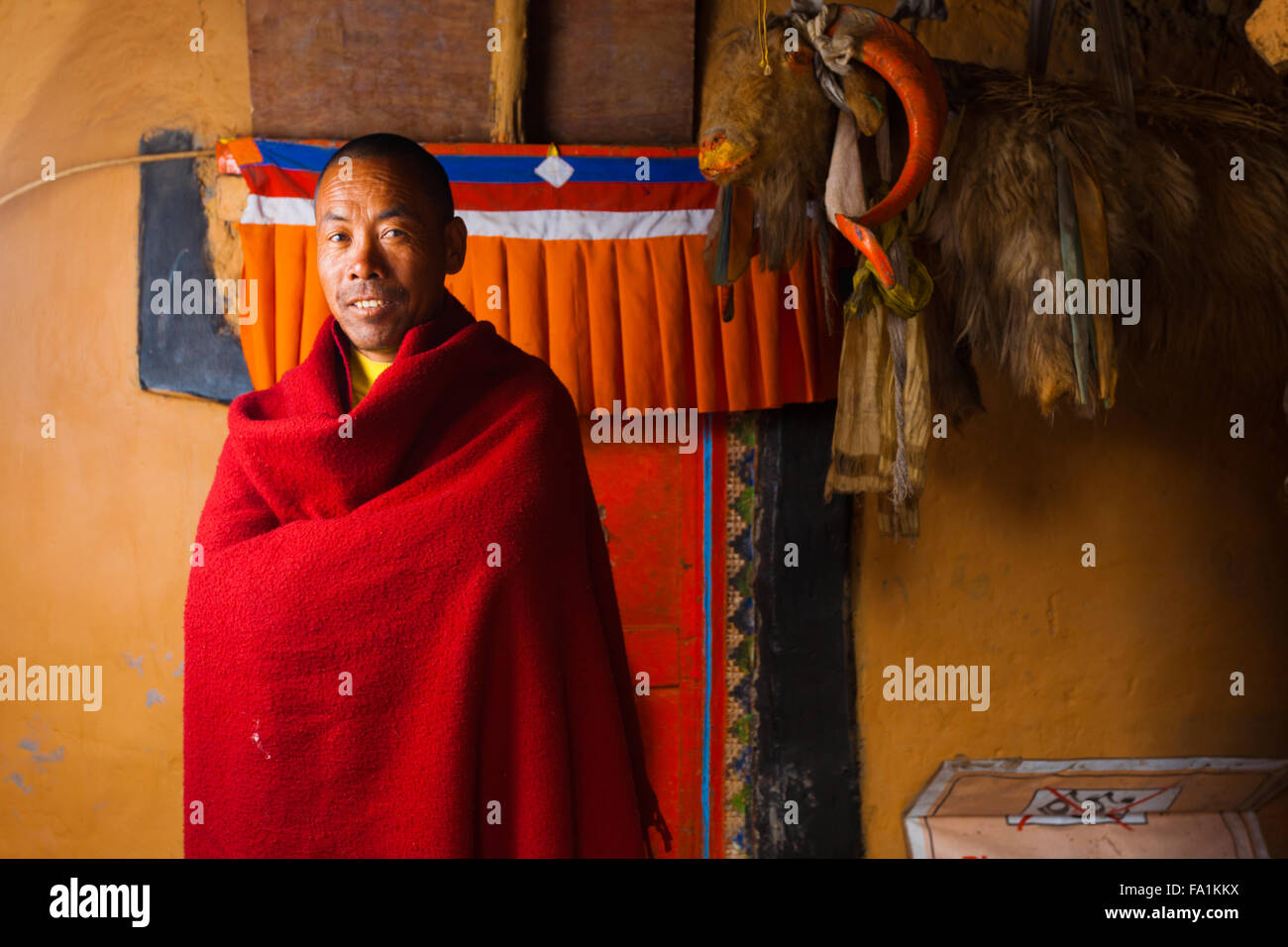 Sorridente, etnicamente monaco tibetano in piedi nel cortile interno contro la parete colorata del vecchio monastero Dhankar in Spiti Valley Foto Stock