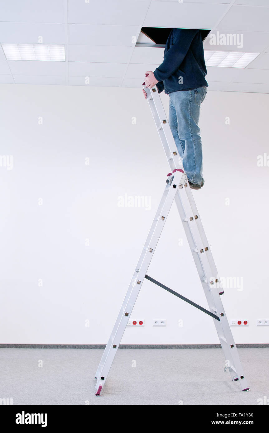 Lavoratore su una scala, il peering attraverso un foro nel soffitto Foto Stock