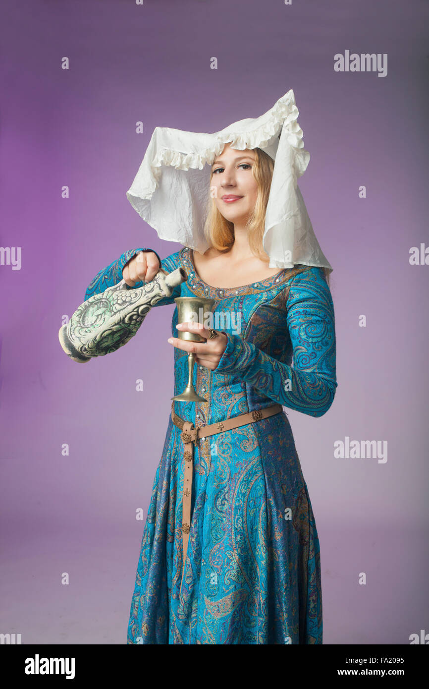 Studio shot della bella ragazza vestita come una dama medievale versando un drink su sfondo viola Foto Stock