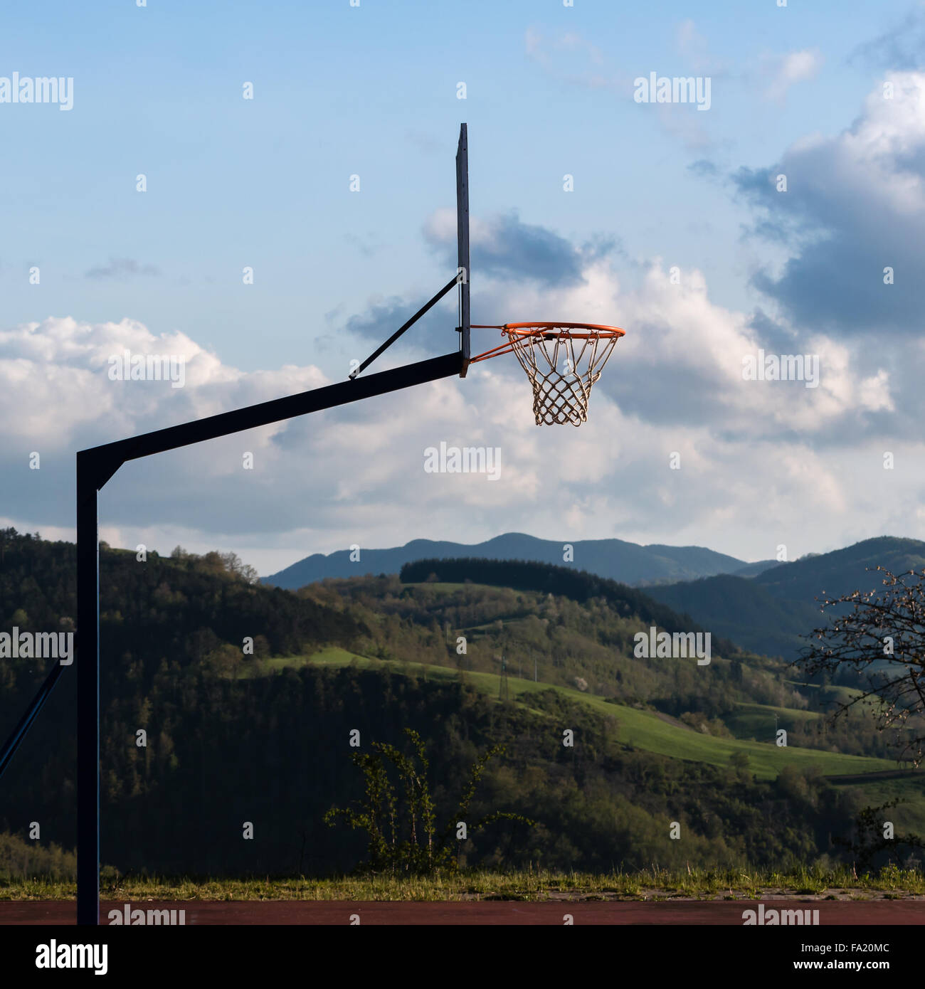 Outdoor Basketball hoop in tribunale, piccola collina e cielo molto nuvoloso in background Foto Stock