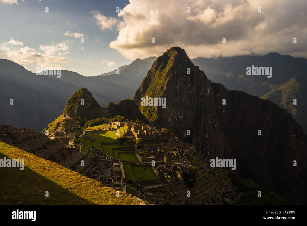 Machu Picchu parzialmente illuminata dall'ultima luce del sole. Ampio angolo di vista dalle terrazze con scenic sky e incandescente sentiero Foto Stock