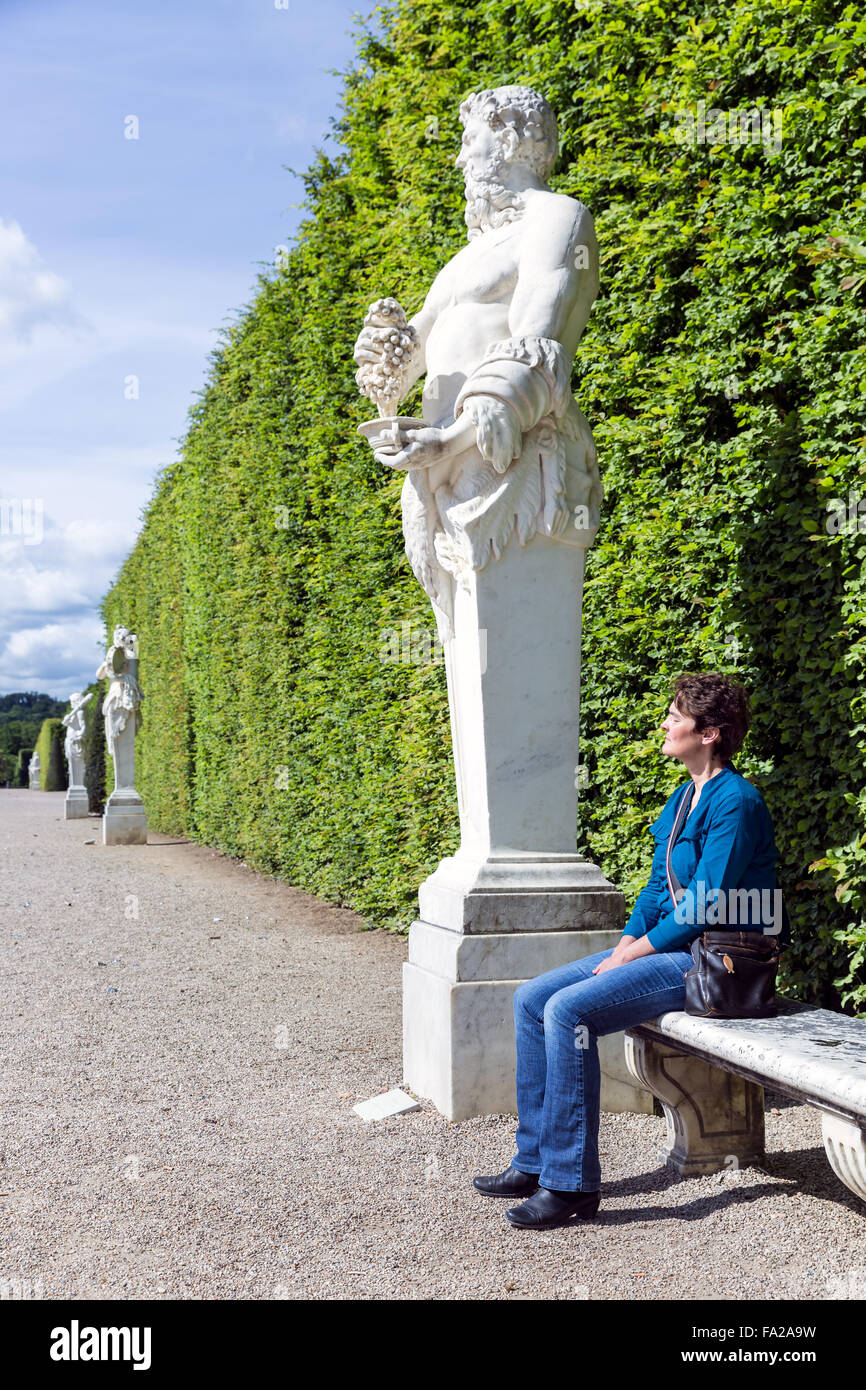 La donna è seduta lungo un sentiero con statue ornamentali nel giardino della Reggia Versailles vicino a Parigi, Francia Foto Stock