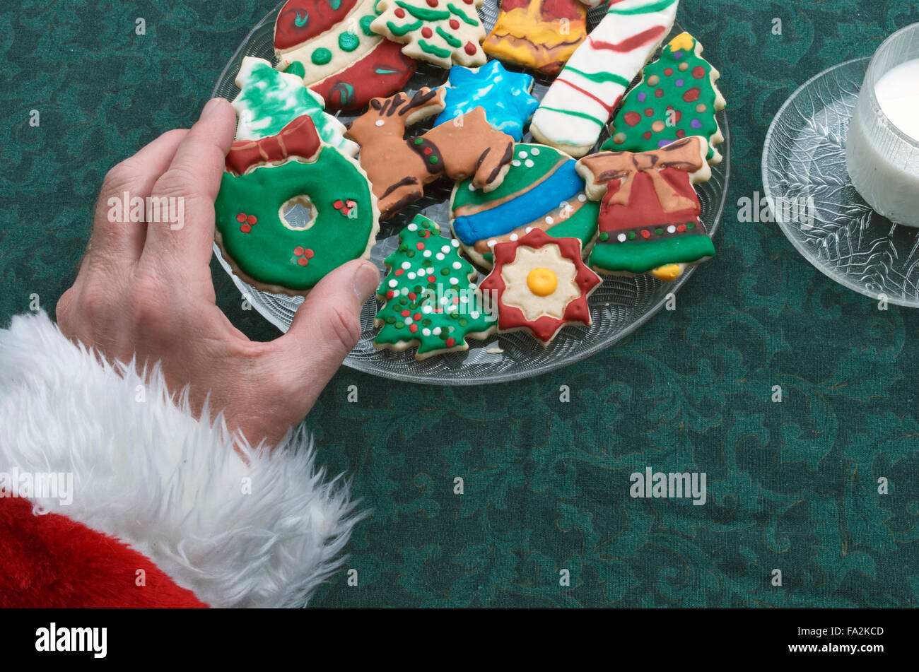 Santa selezionando un ritaglio di Natale Cookie Off della piastra, con un bicchiere di latte Foto Stock