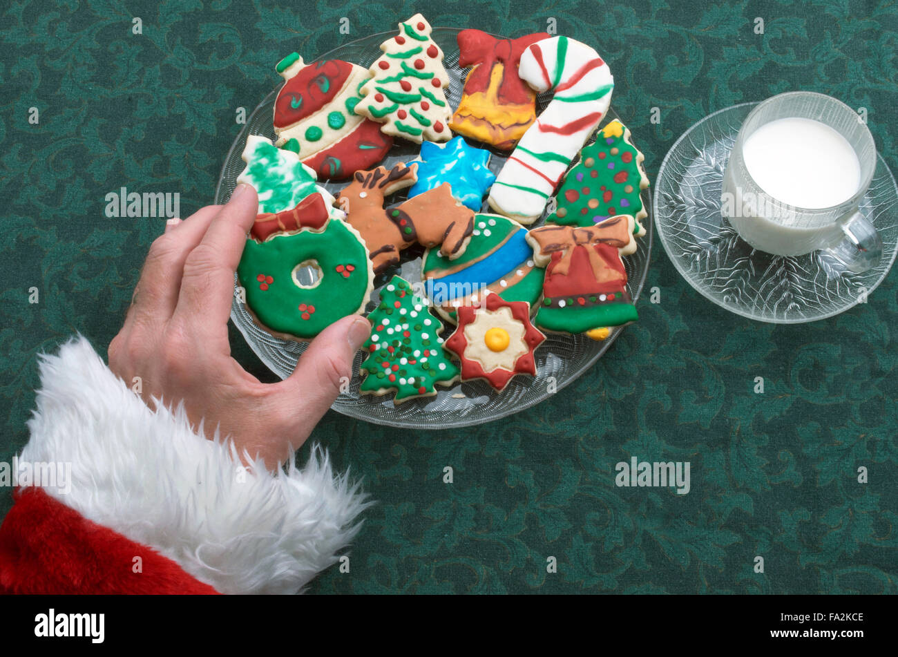 Santa selezionando un ritaglio di Natale Cookie Off della piastra, con un bicchiere di latte Foto Stock