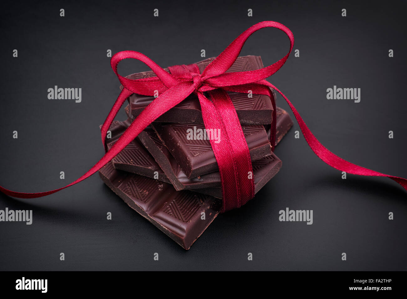 Cioccolato fondente con nastro rosso su sfondo nero. Close up. Foto Stock