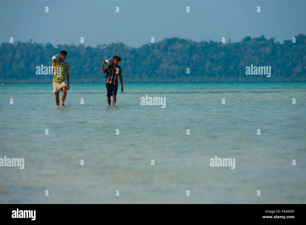 Indian dive lavoratori portano le immersioni serbatoi di ossigeno in un mare poco profondo e di limpide acque turchesi Foto Stock