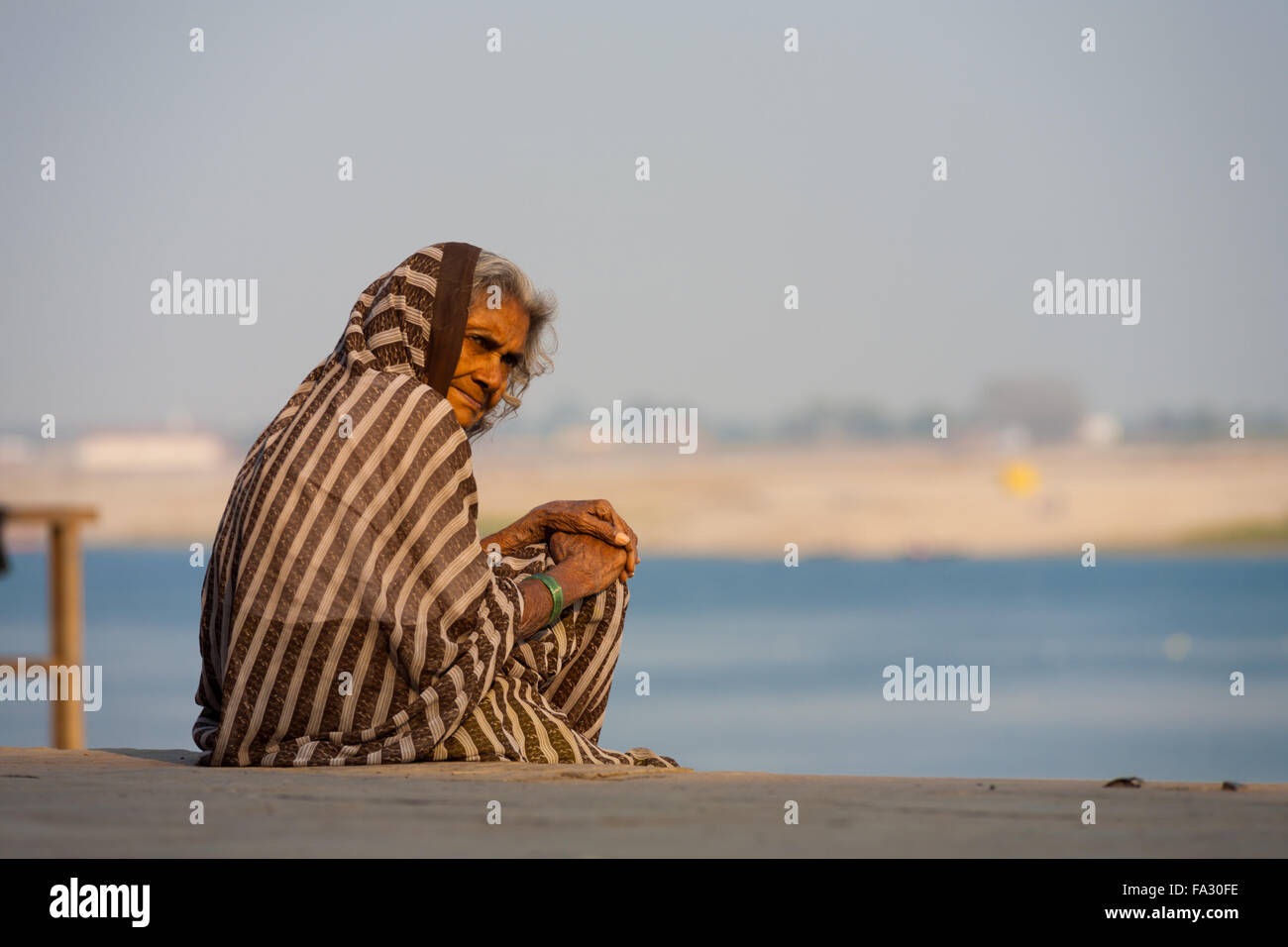 Donna indiana in marrone saree, scialle seduta su riverside ghat al di fuori del suo ospizio Foto Stock