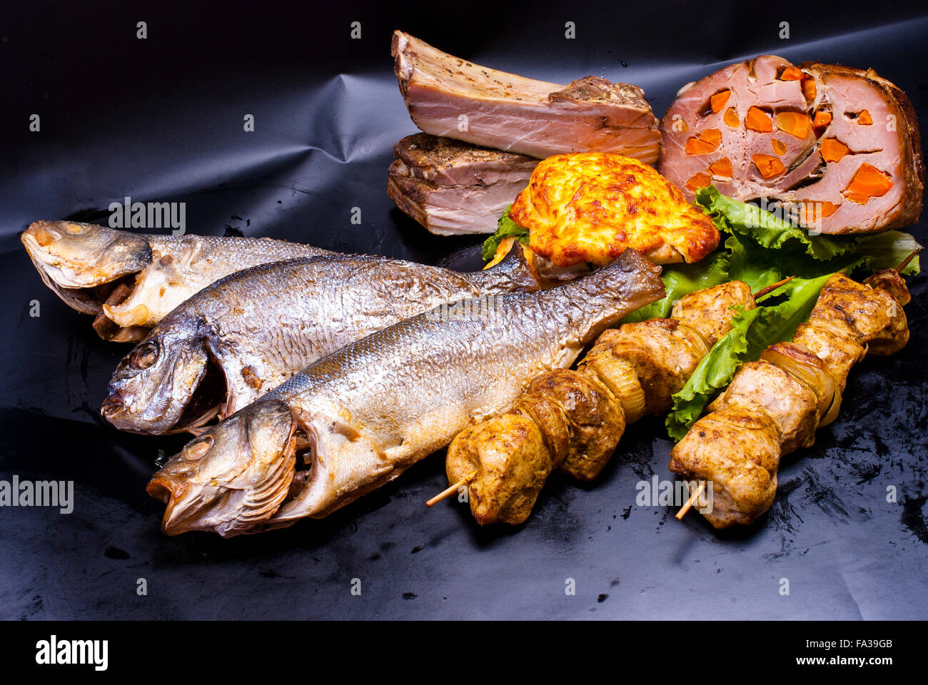 Still Life - carne con ripieni, shish kebab, bistecca in pastella, crepes con ripieni, pesce fritto su sfondo nero Foto Stock