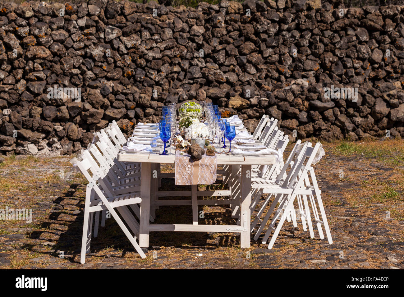 White tavolo e sedie di legno insieme con gli occhiali blu, fiori e decorazioni per una celebrazione all'esterno. Foto Stock