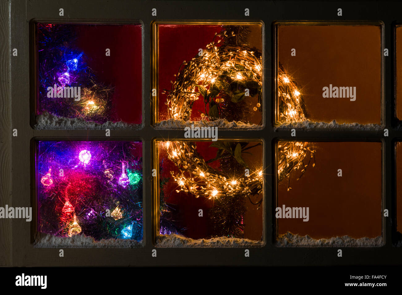 Ghirlanda illuminato e albero di Natale luci attraverso una finestra lodge, con la neve. Foto Stock