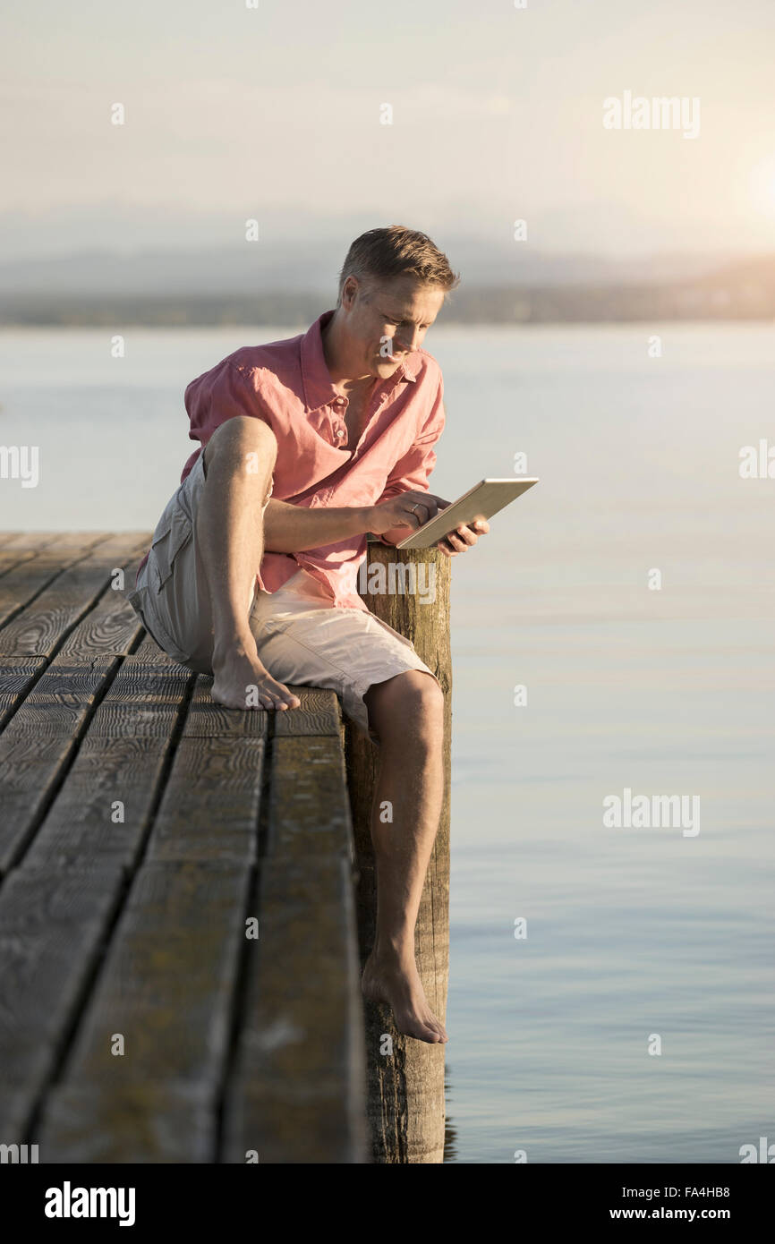 Uomo maturo con tavoletta digitale sul molo del lago, Baviera, Germania Foto Stock