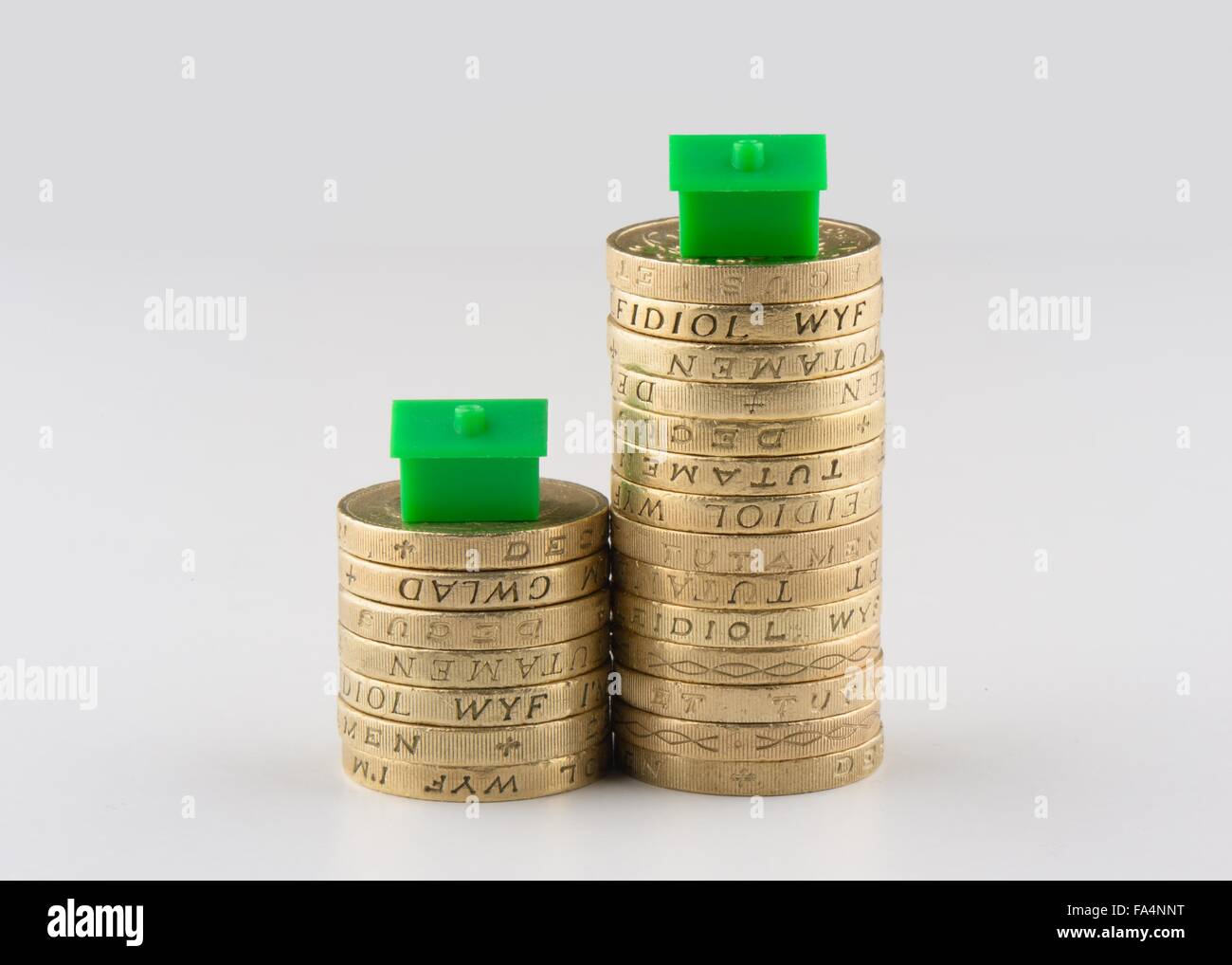 Due pile di UK pound monete con case in plastica sulla parte superiore suggestivo di ridimensionamento o il mercato immobiliare. Foto Stock