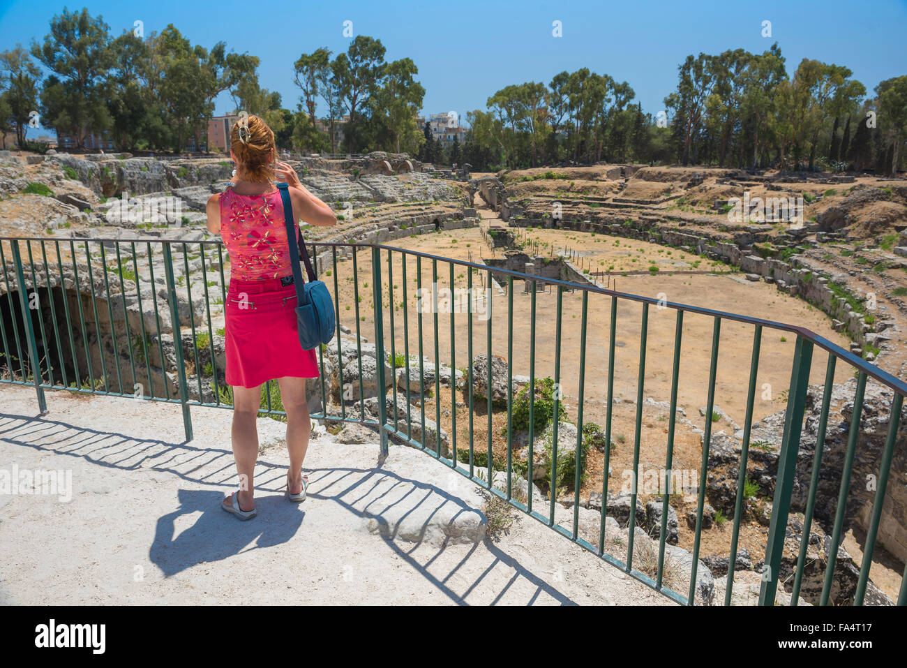 Donna solista turistica, vista posteriore di una femmina matura turistica prendendo una foto dell'anfiteatro romano rovine nel parco archeologico di Siracusa, Sicilia Foto Stock