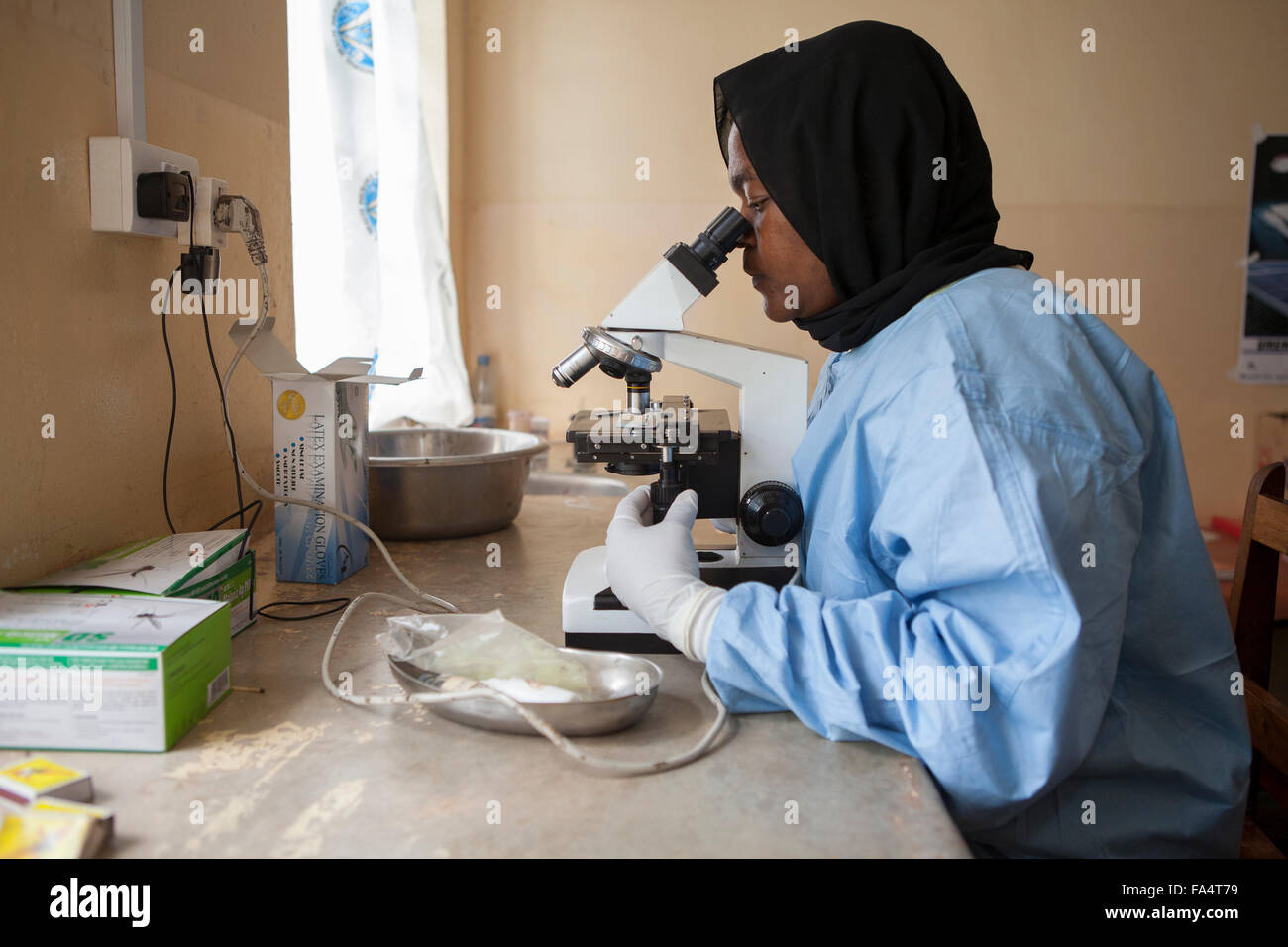 Un assistente di laboratorio opera un microscopio a energia solare di centro di salute della regione di Kigoma, Tanzania occidentale. Foto Stock