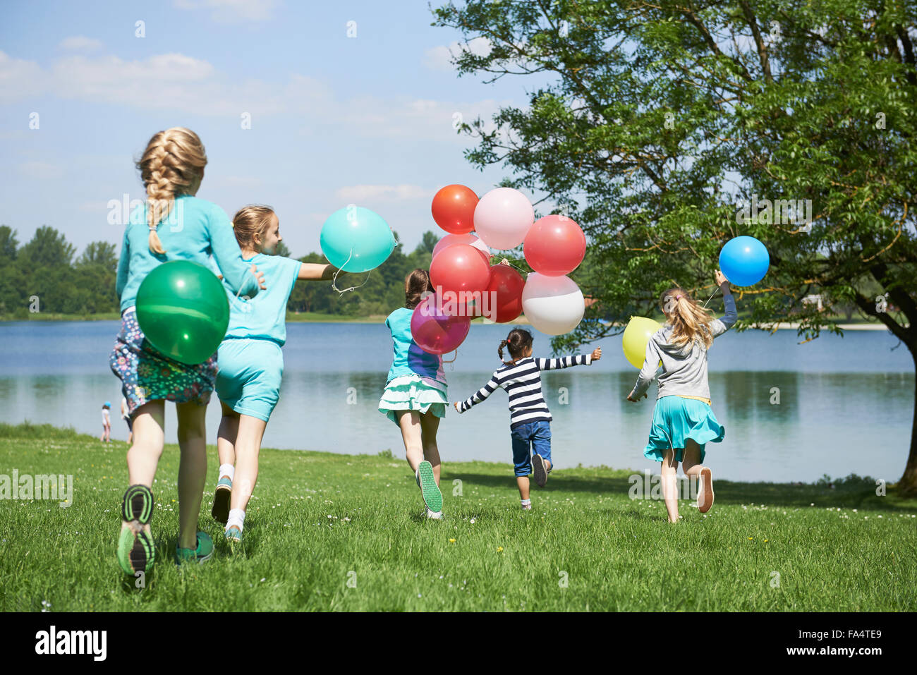 Vista posteriore di ragazze in esecuzione nel parco con palloncini, Lago Karlsfeld di Monaco di Baviera, Germania Foto Stock