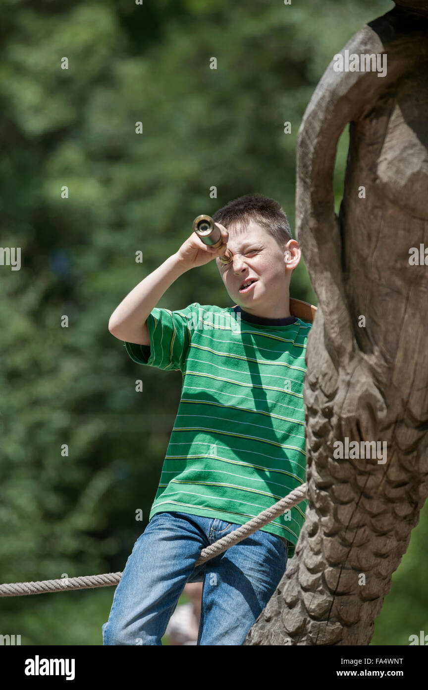 Ragazzo in piedi su una nave e guardando attraverso un telescopio nel parco giochi avventura, Baviera, Germania Foto Stock