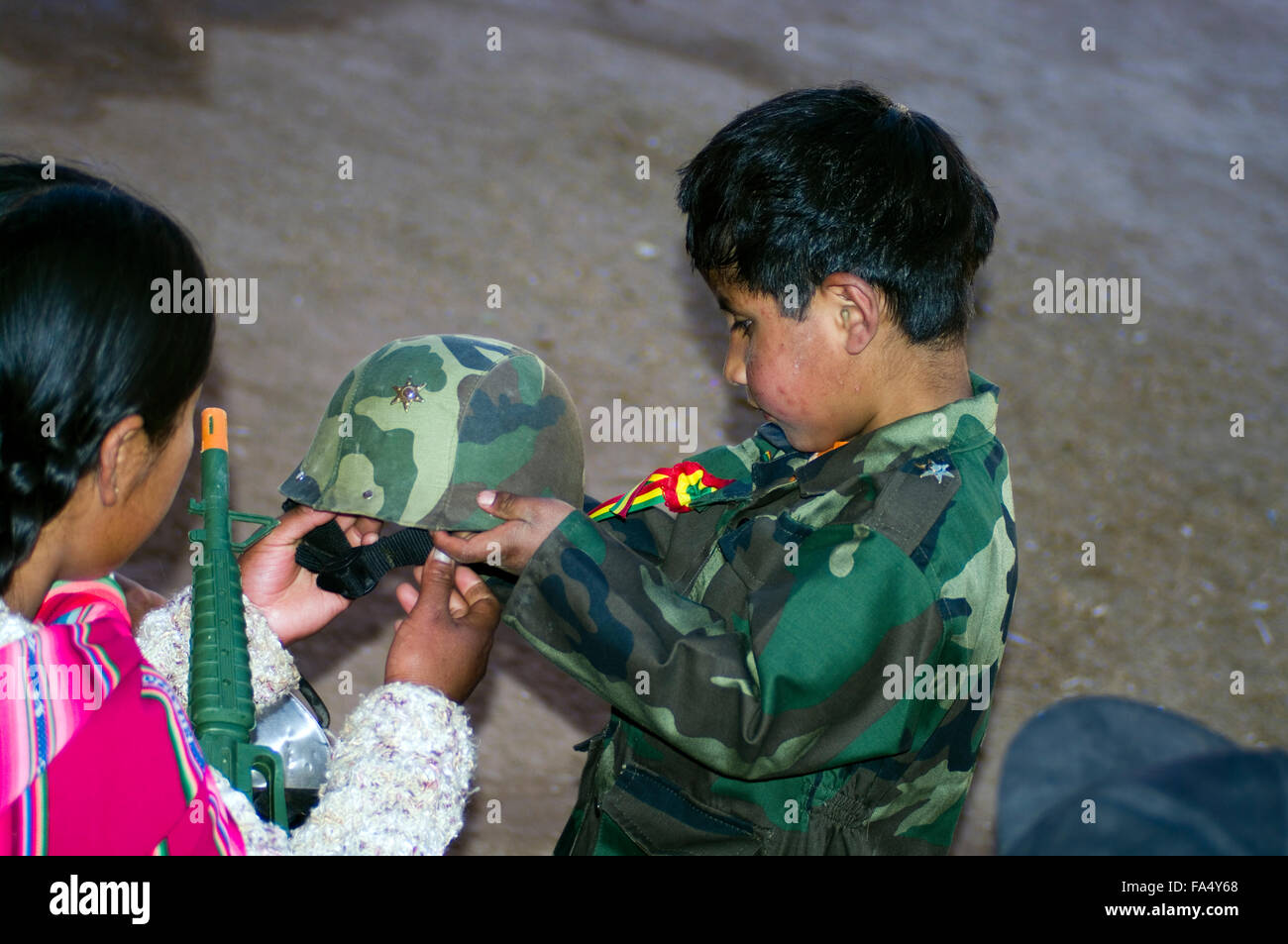 Ragazzo boliviano in soldier uniformi della preparazione a don il suo casco mentre sua madre assiste. Foto Stock