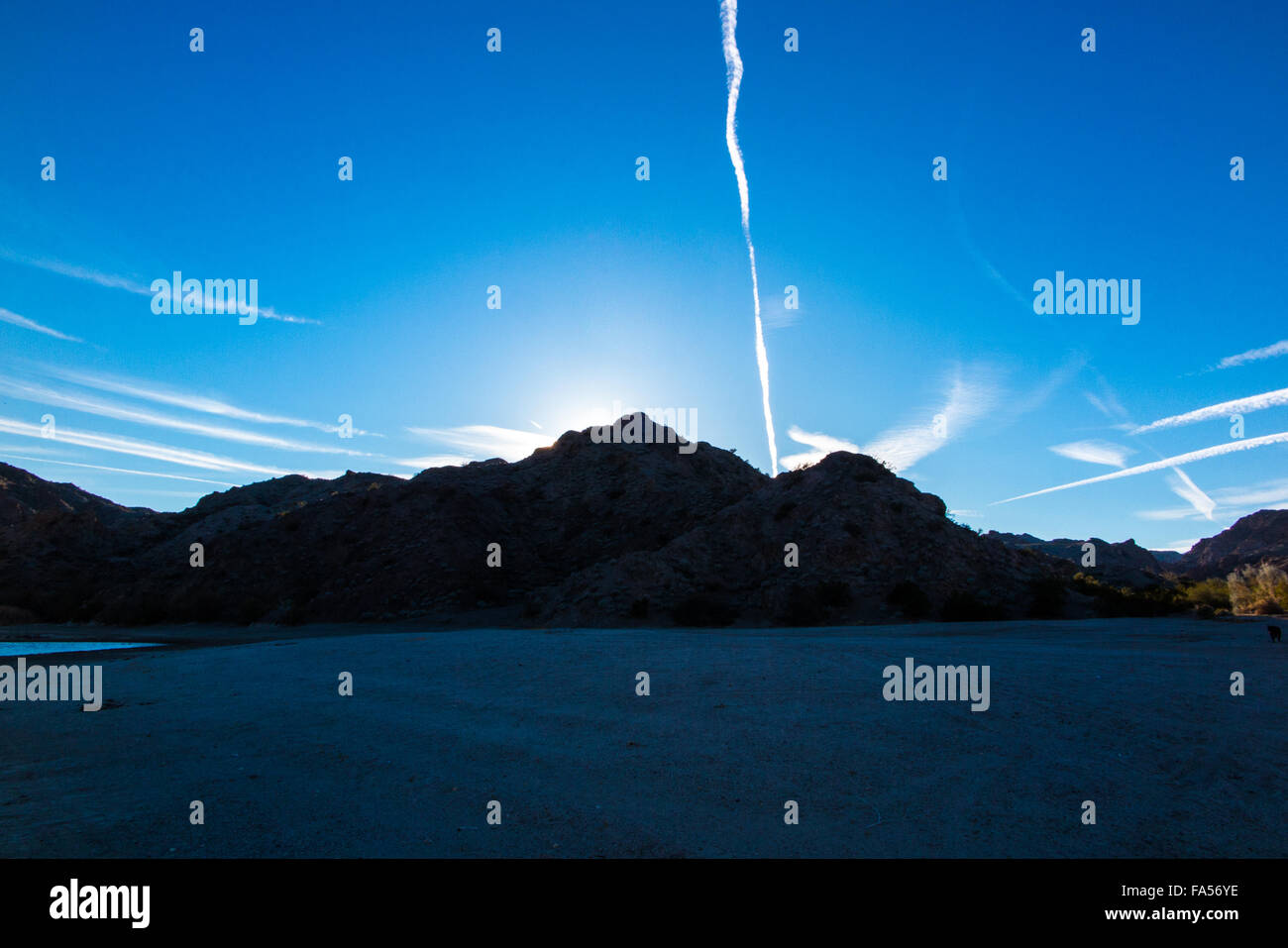 Il sole tramonta sul lago Mohave nel deserto del Nevada con un cielo pieno di contrails dal passaggio dei getti. Foto Stock
