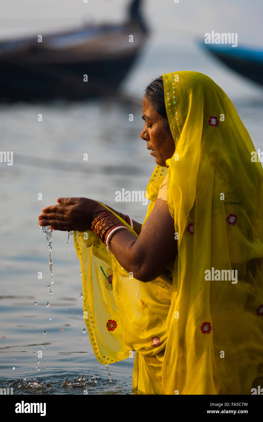Devota donna indù in giallo saree coppettazione acqua nelle mani di pregare e di balneazione, una importante tradizione culturale, nel fiume Gange Foto Stock
