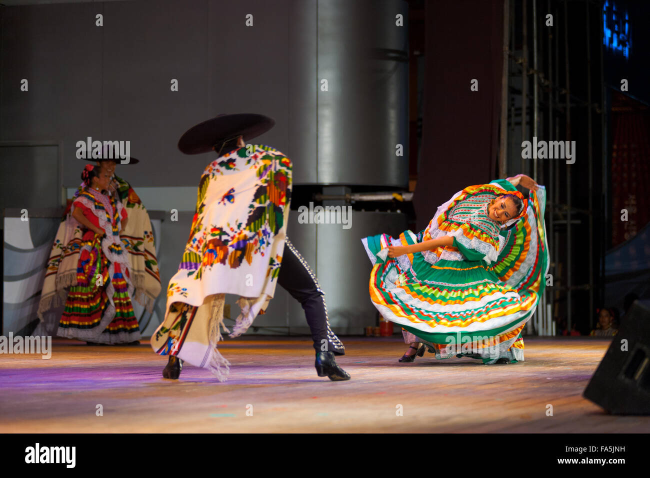 Ballerino femmina indossando variopinti abito verde, piegando lateralmente il corpo danza con partner di sesso maschile in capo durante un ballo messicano Foto Stock