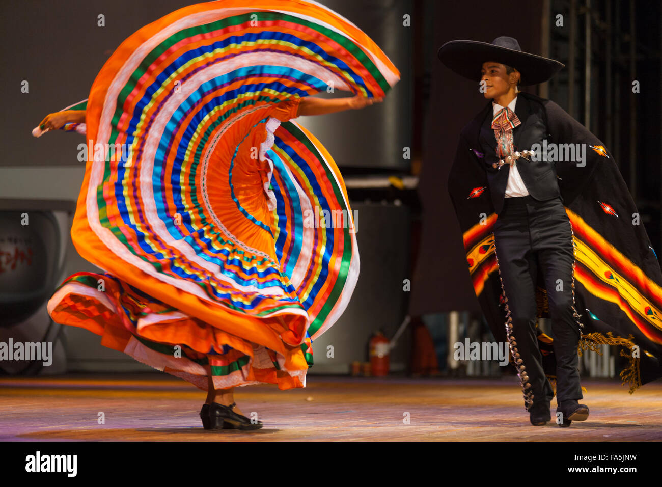 Uomo che indossa gli abiti tradizionali di danza Mexican Hat dance con la donna flailing il suo abito arancione nel modello in un folk show a un Foto Stock