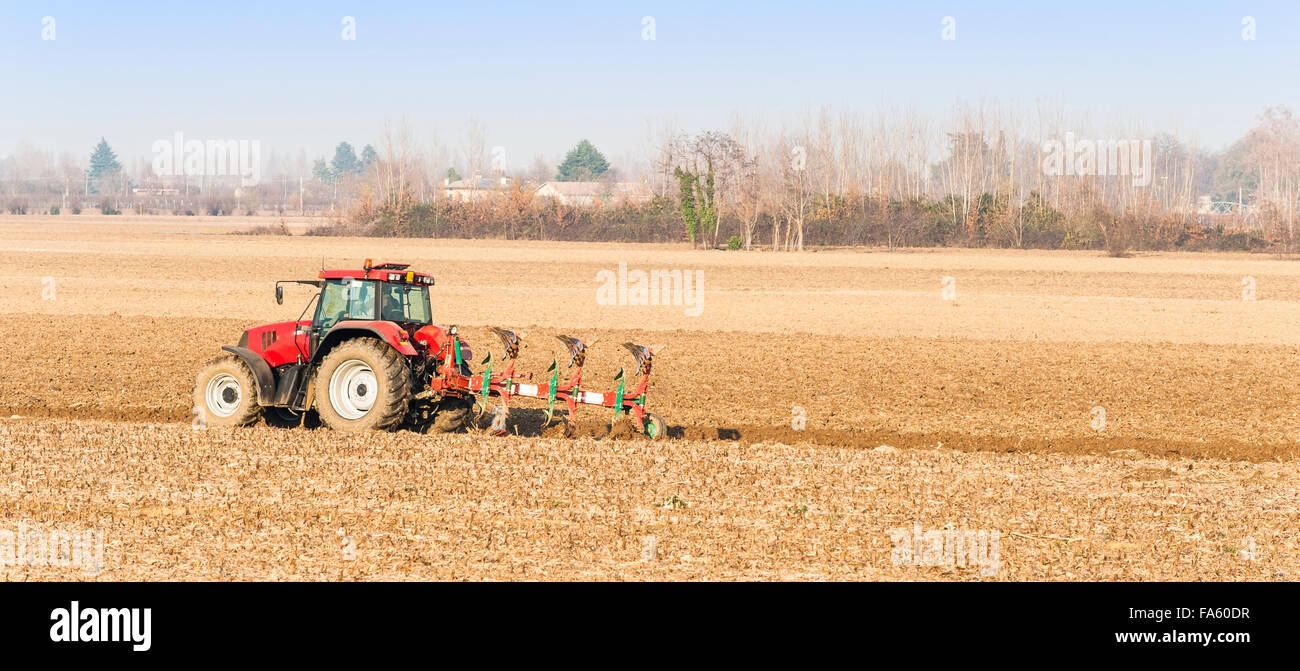 Manodopera agricola, Trattore rosso arando un campo Foto Stock