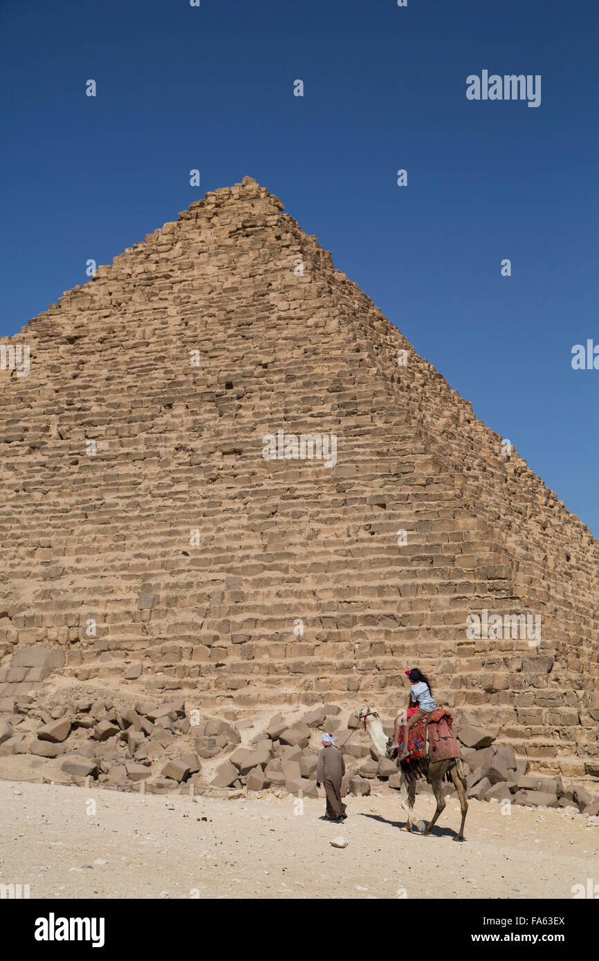 Uomo che cammina cammello con Tourist, piramide di Mycerinus (fondo), le Piramidi di Giza, Giza, Egitto Foto Stock