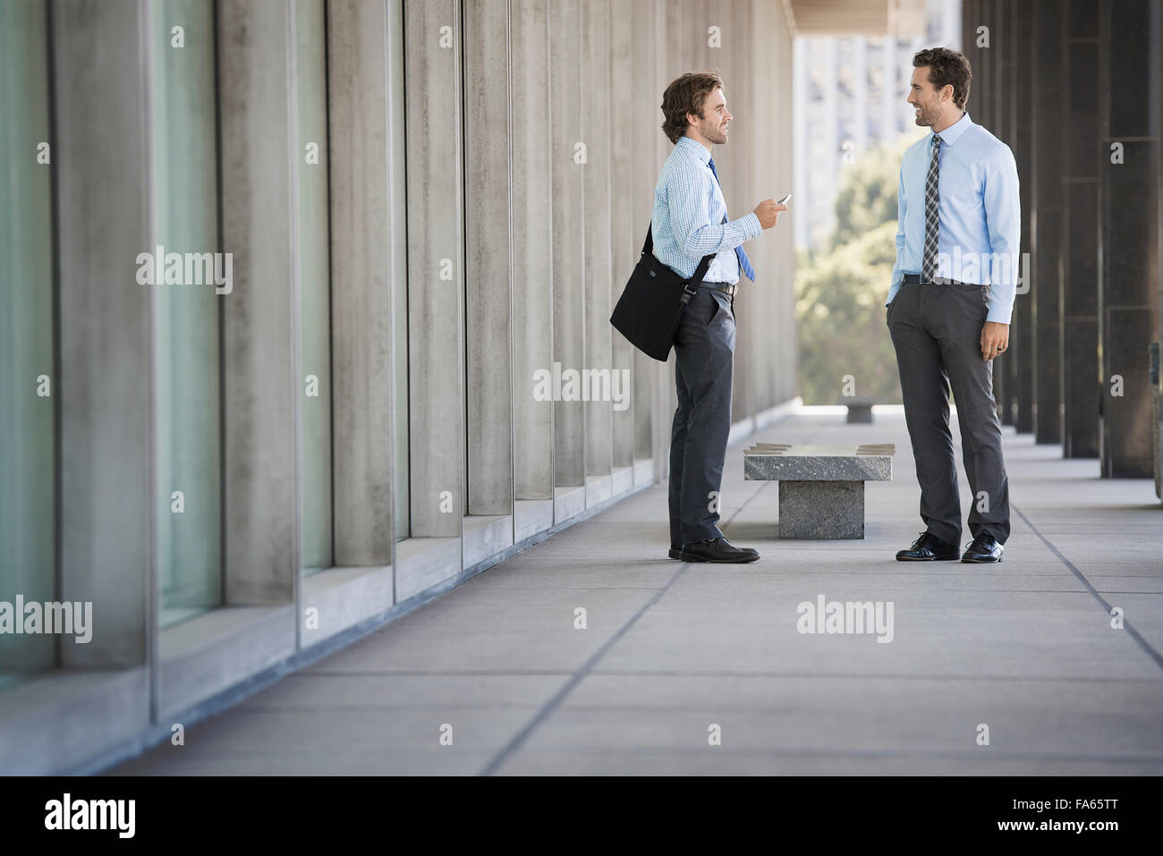 Due imprenditori su una passerella al di fuori di un edificio, parlando. Foto Stock