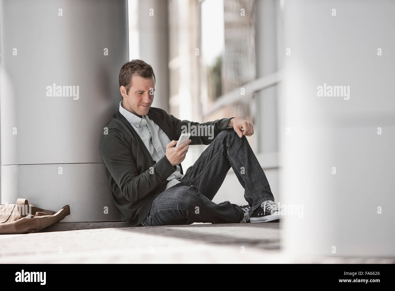 Un uomo al di fuori di un edificio, controllando il suo smart phone. Foto Stock