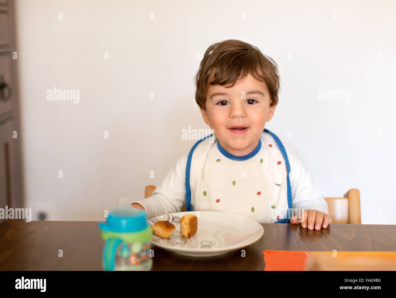 Sorridente ragazzo seduto a tavola a mangiare snack Foto Stock