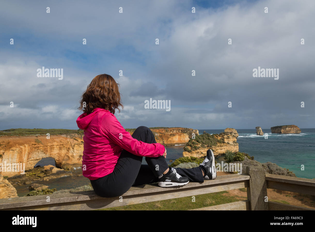 Vista laterale della donna seduta sulla parete, Port Campbell, Victoria, Australia Foto Stock