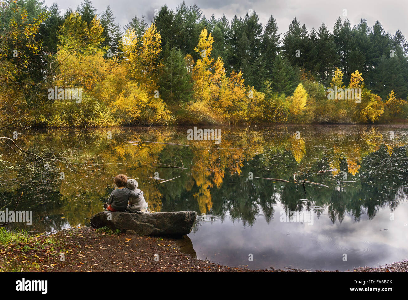 Un ragazzo e una ragazza seduta su una roccia da un lago Foto Stock