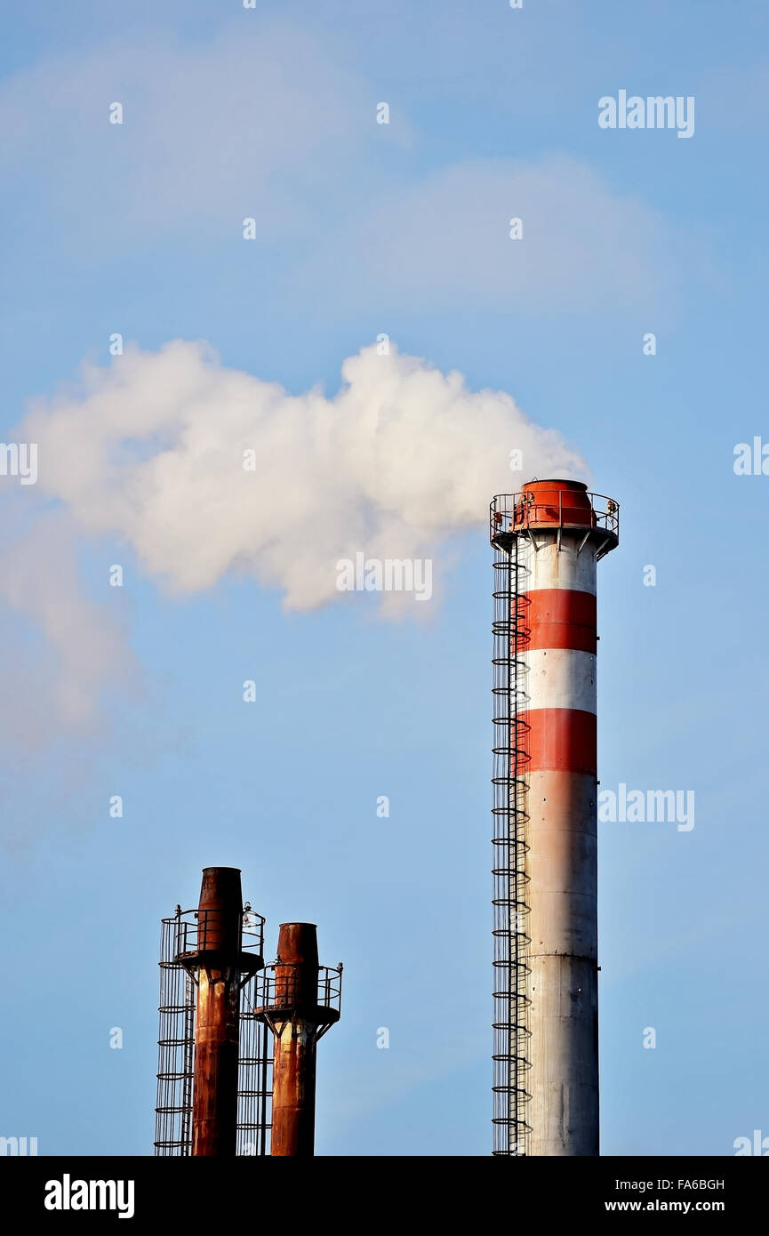 Il fumo e il vapore che fuoriesce da un industriale impianto petrolchimico camino con un cielo blu sullo sfondo Foto Stock