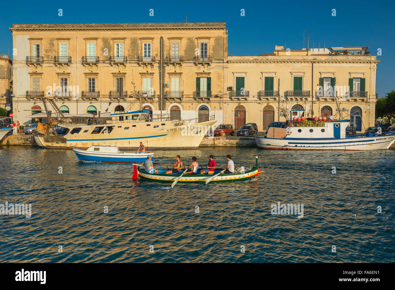 Uomini canottaggio Mediterraneo, vista di una squadra di canottaggio che si dirige su uno stretto canale che separa Ortigia dalla città di Siracusa, Sicilia. Foto Stock