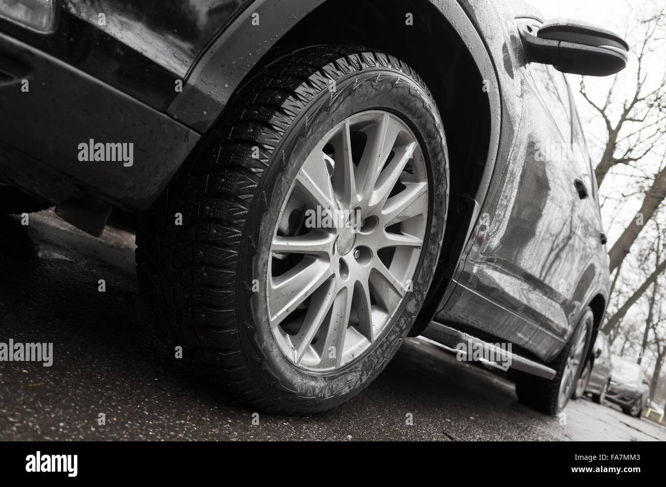 Primo piano ad angolo ampio frammento foto di auto nera, ruota in lega leggera con pneumatici invernali sulla città sporca road. Messa a fuoco selettiva e dovrà Foto Stock