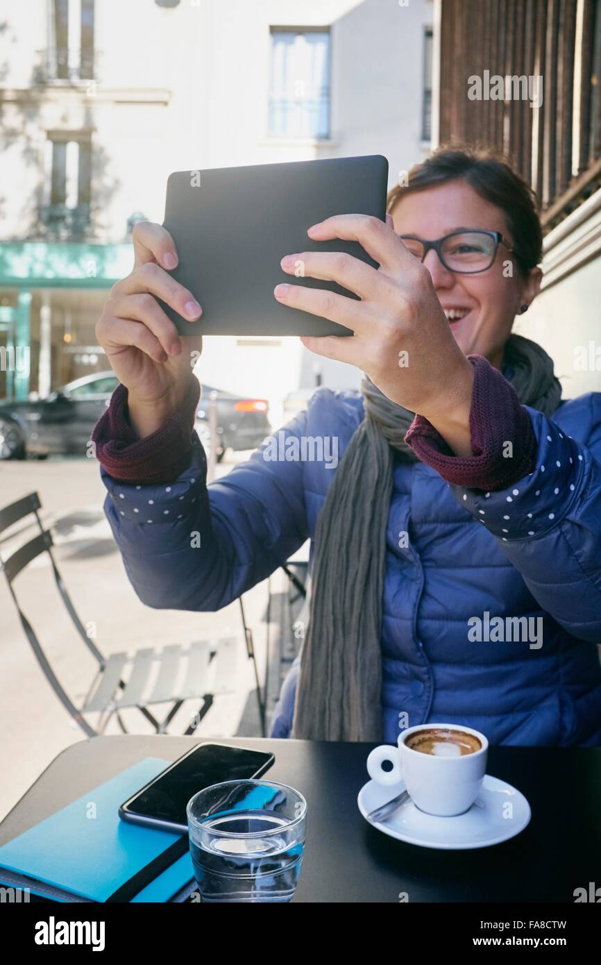 Metà donna adulta prendendo tavoletta digitale selfie al cafè sul marciapiede Foto Stock