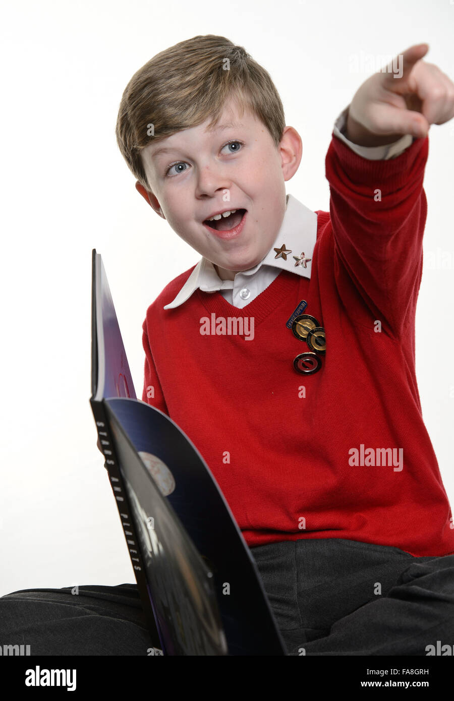 Un giovane (scuola primaria) ragazzo in un rosso uniforme scolastica maglione libri di lettura e scrittura di note per i suoi compiti. Foto Stock