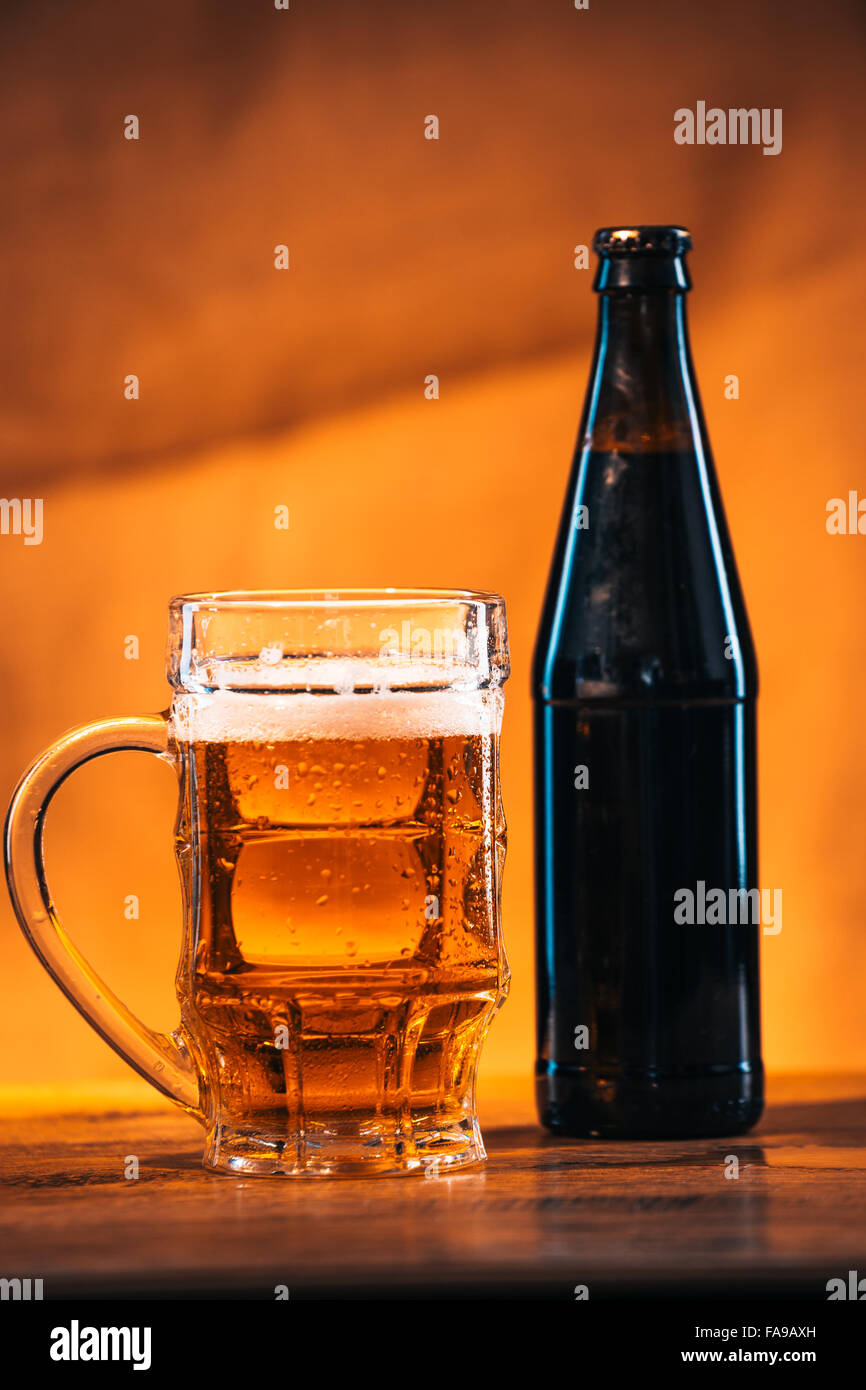 Bottiglia e bicchiere di fresca birra luminoso con formaggio affumicato intreccio sul tavolo di legno Foto Stock