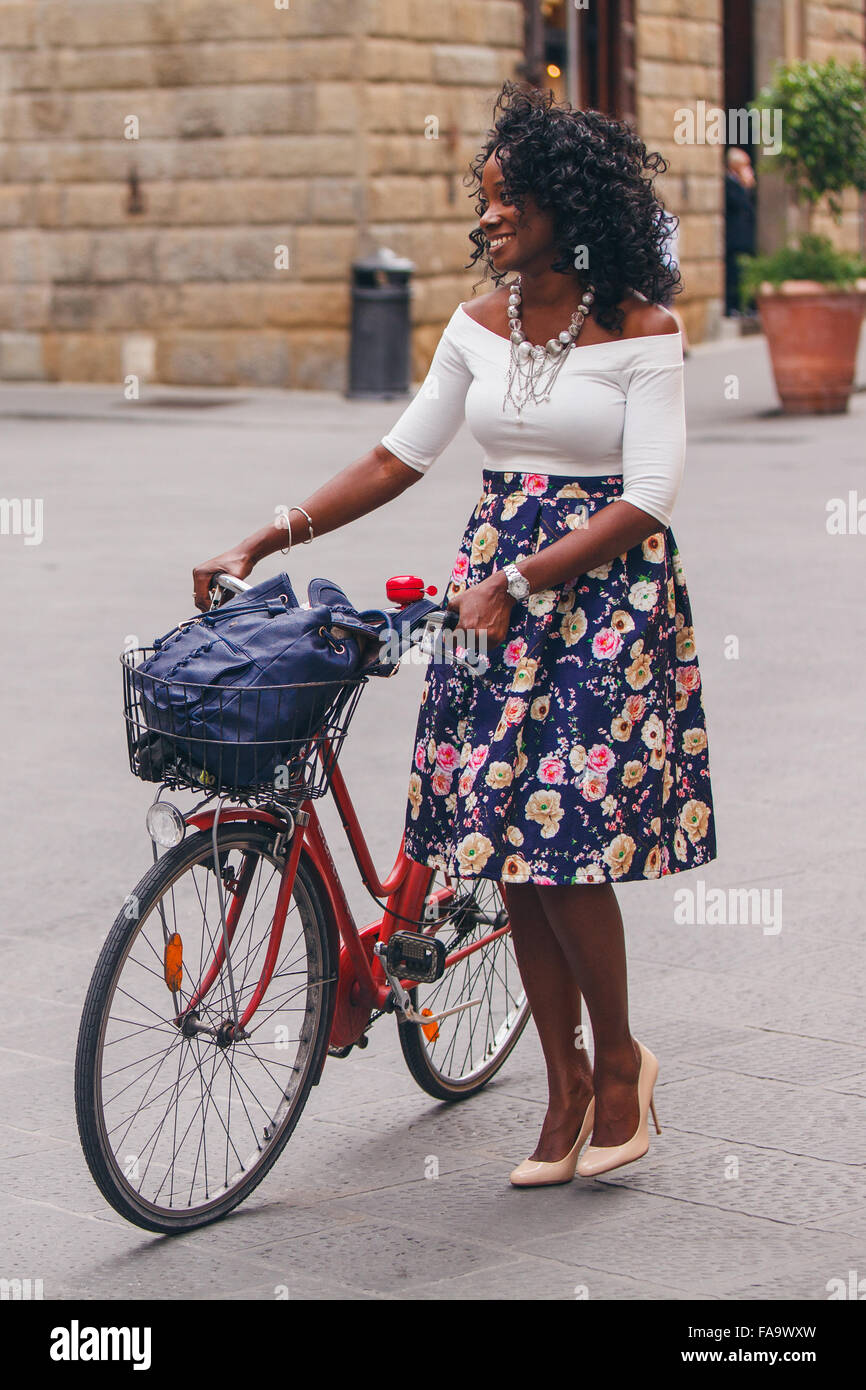 Capelli ricci moda donna che cammina con una bici rossa Foto Stock