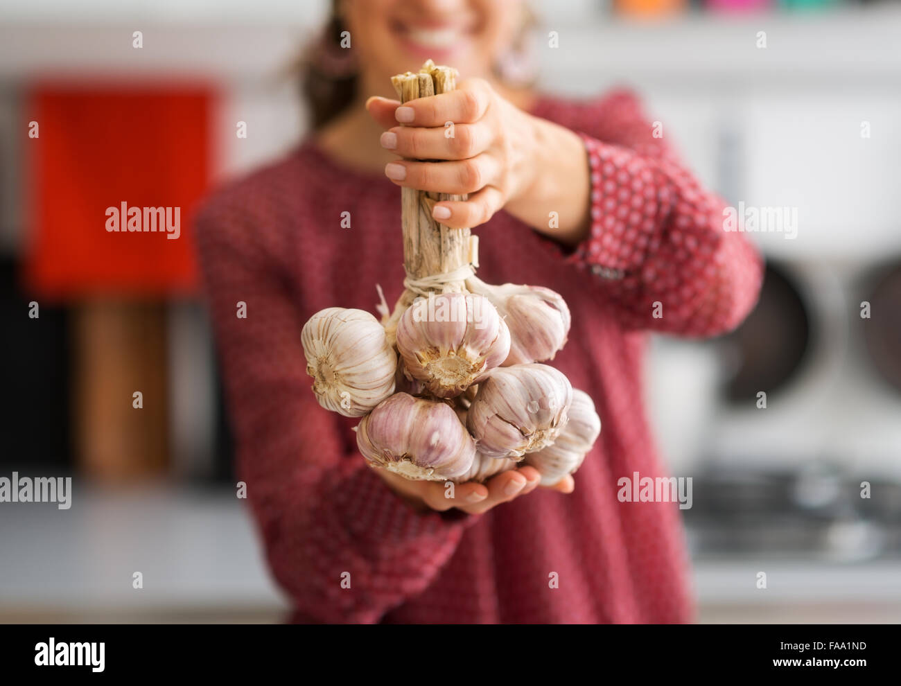 Un mazzetto di capi di aglio sono legati insieme. Sorridente, una donna in background li tiene in alto. Foto Stock