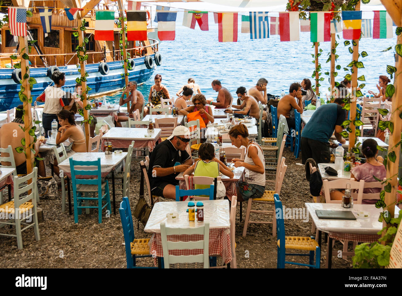 Santorini, Korfos, Cadouni, café, il ristorante sulla spiaggia. Affollate di turisti seduti ai tavoli e sedie per mangiare sotto la fila di mini bandiere nazionali. Foto Stock