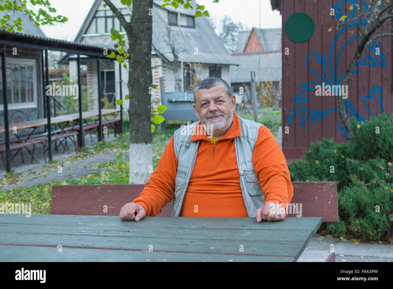 Uomo anziano seduto su una panchina vicino casa in legno in serata autunnale Foto Stock