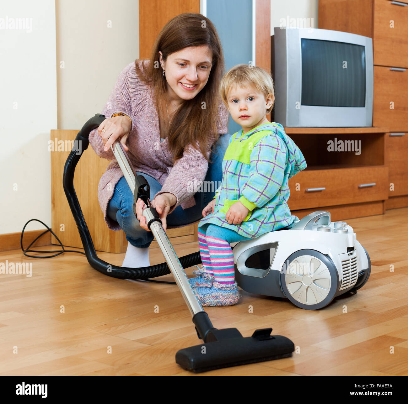 Felice casalinga con un bimbo di pulizia stanza vivente con aspirapolvere Foto Stock