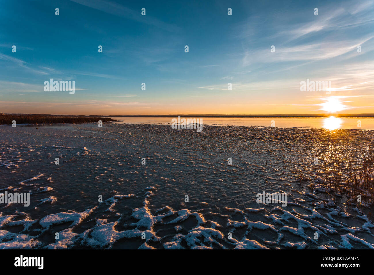 Sun riguarda l'orizzonte sulla costa d'inverno, che viene riflesso dall'acqua e ghiaccio. Foto Stock